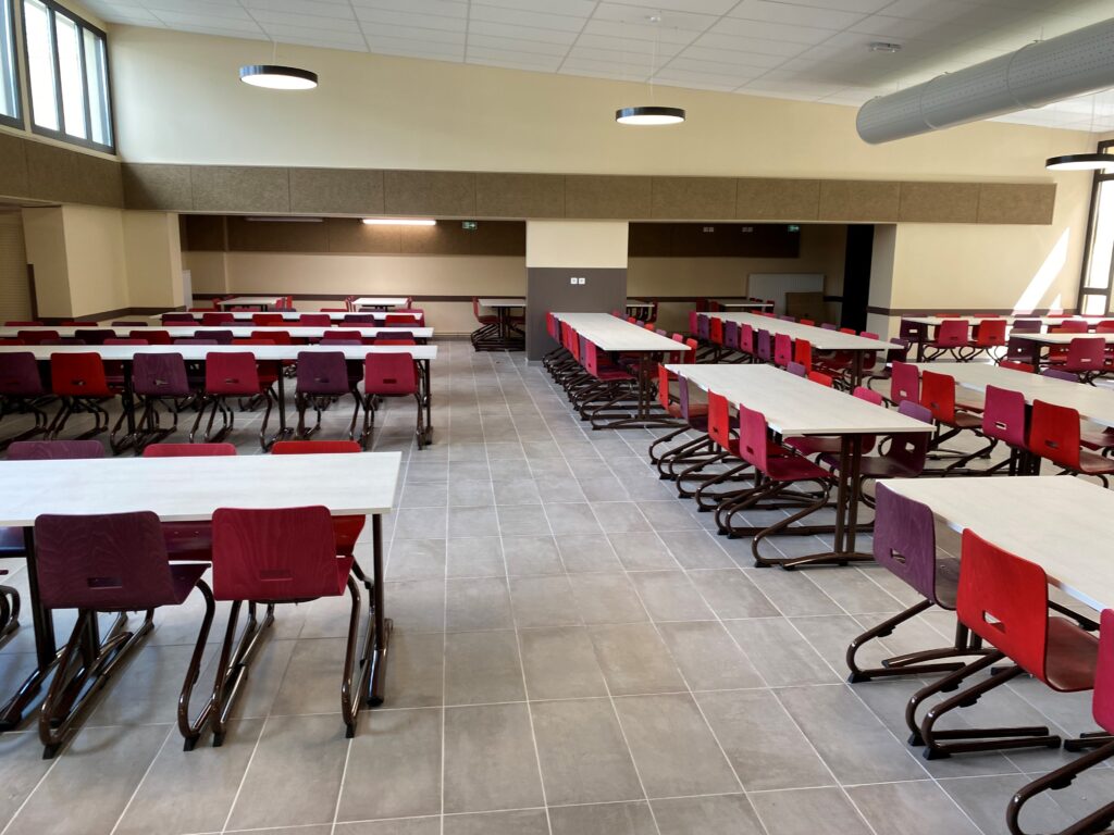 Cafétéria moderne : Design épuré, tables et chaises colorées Grande cafétéria moderne vide avec rangées de tables blanches, chaises rouges et violettes à piètement métal. Lumière naturelle, spots ronds et panneaux muraux.