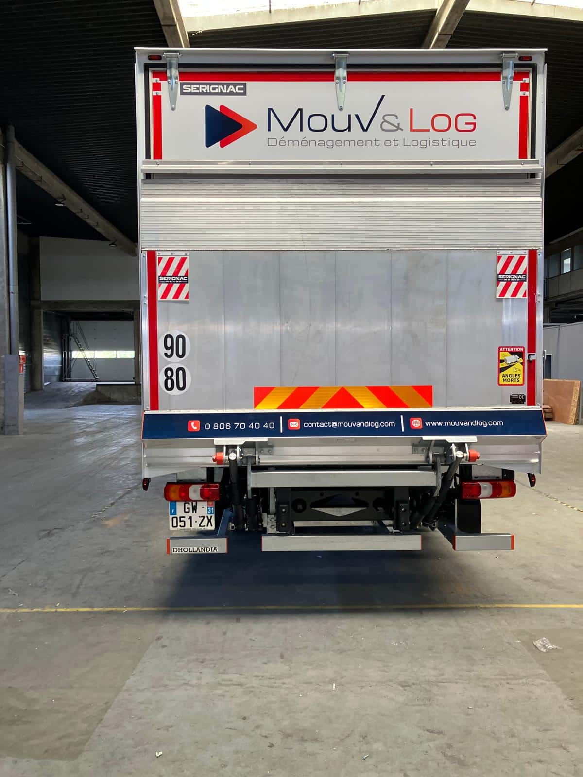 Arrière d'un camion de déménagement Mouv&Log en entrepôt, affichant contacts (tél, mail, web), vitesses 90/80, et avertissement angles morts.