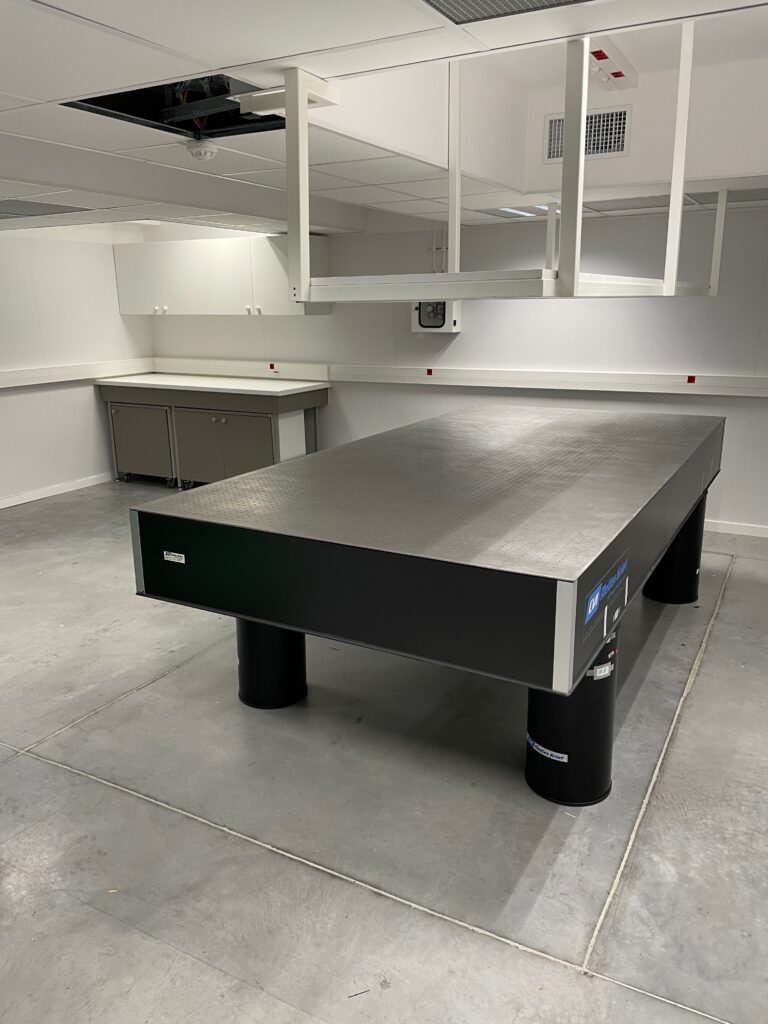 Laboratoire Moderne: Table Optique CVI Melles Griot Laboratoire moderne et propre avec grande table optique CVI Melles Griot grise et noire sur pieds cylindriques, comptoirs et armoires.