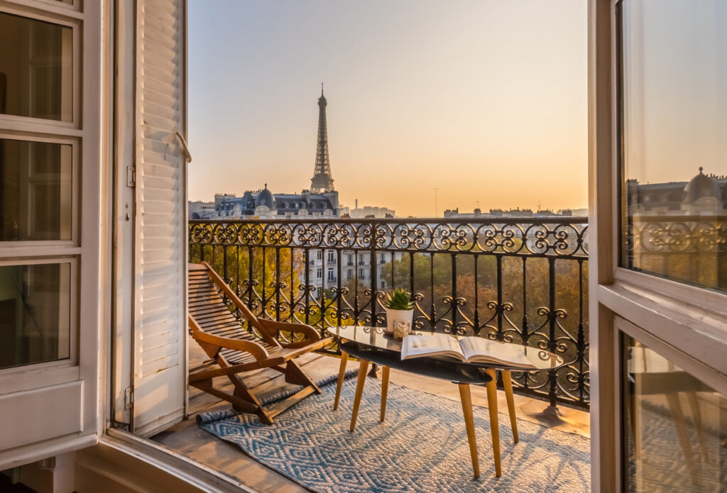 Balcon Parisien : Vue Époustouflante sur la Tour Eiffel au Coucher Balcon parisien ensoleillé avec vue sur la Tour Eiffel au coucher. Chaise en bois, livre ouvert sur table, ambiance de détente à l'heure dorée.