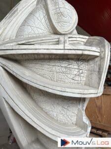 Détail d'une sculpture ou d'un moule en plâtre gris, texturé de fines gravures croisées et de formes courbes, avec un logo "Mouv&Log".